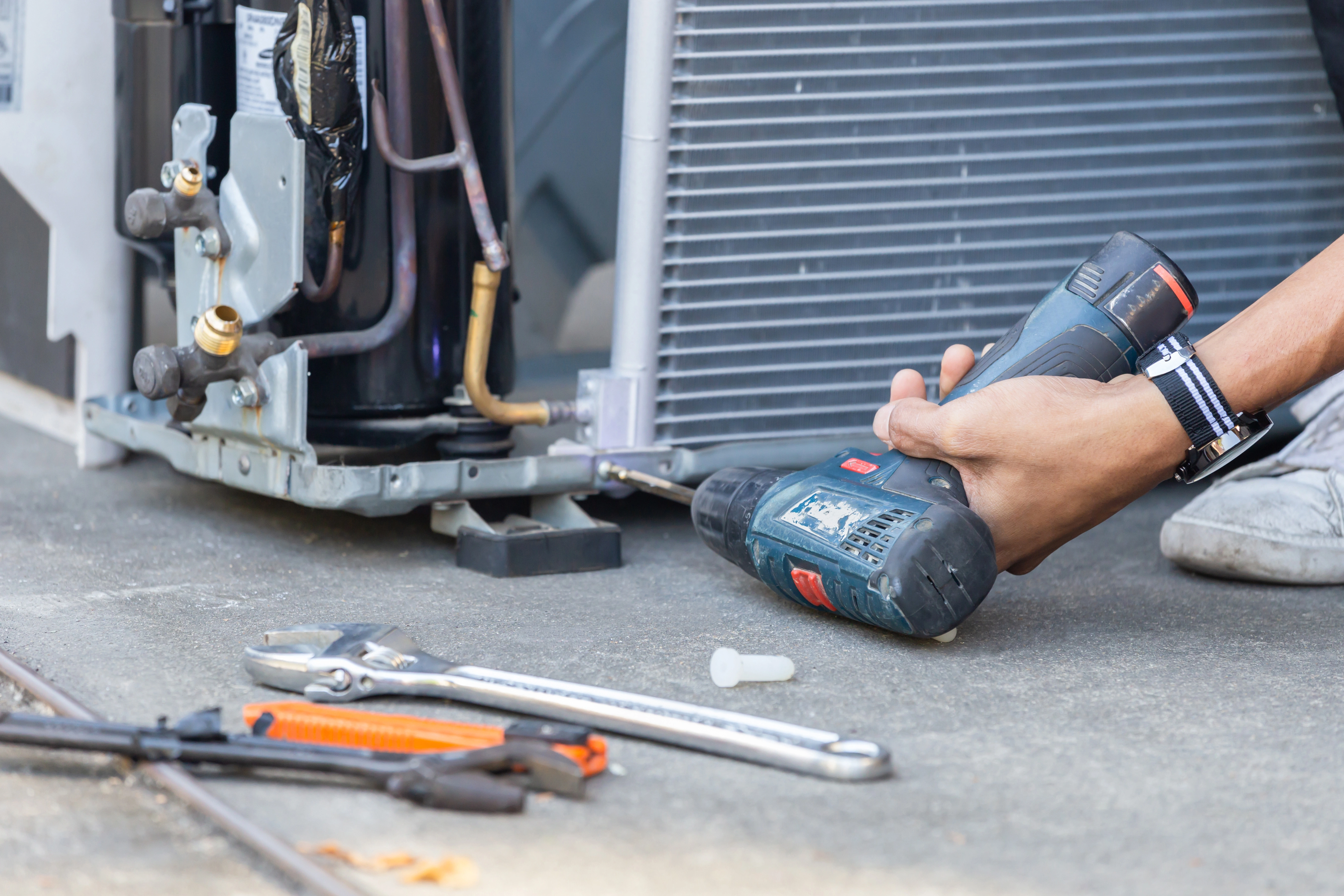 An AC TO THE MAX, INC technician using a drill to assemble an AC compressor for a new installation in Phoenix.